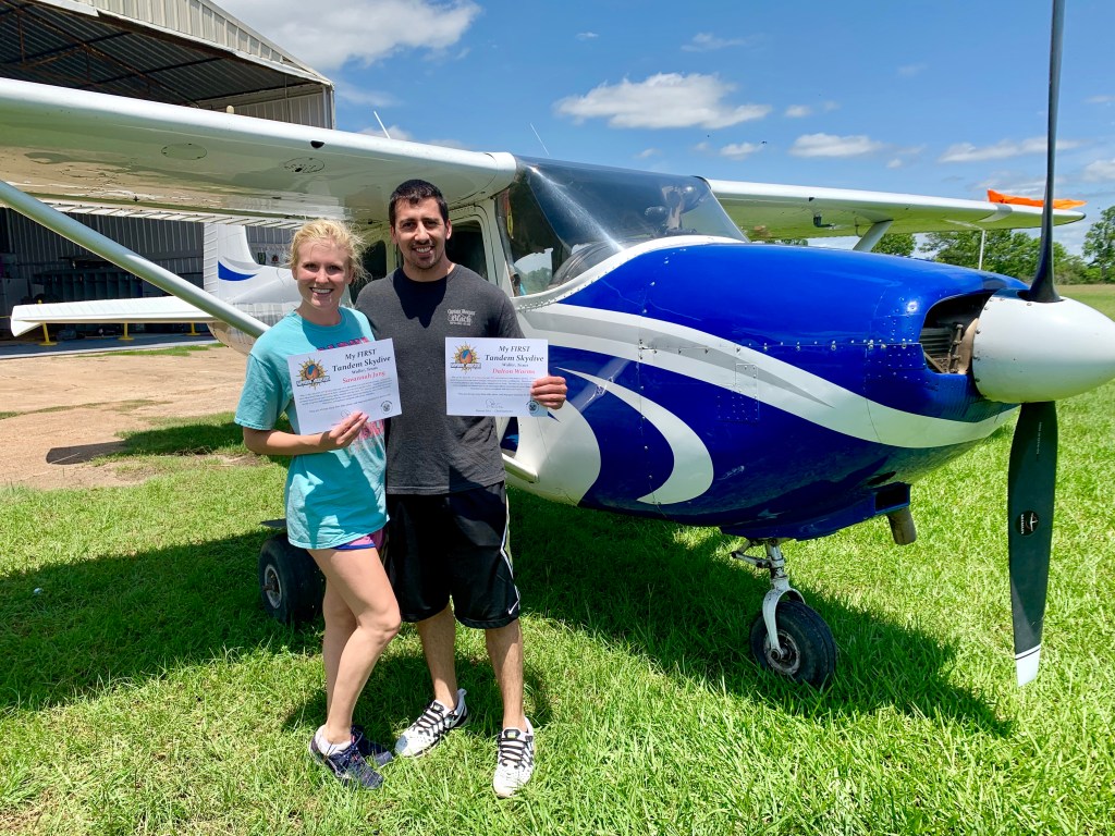 Skydivers standing next to prop plane